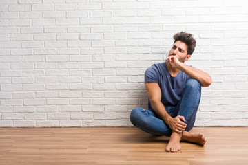 Young natural man sit on a wooden floor doubting and confused, thinking of an idea or worried about something