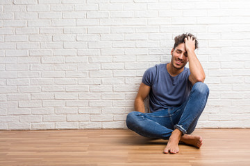 Young natural man sit on a wooden floor laughing and having fun, being relaxed and cheerful, feels confident and successful