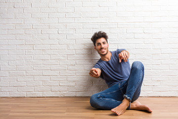 Young natural man sit on a wooden floor cheerful and smiling pointing to the front