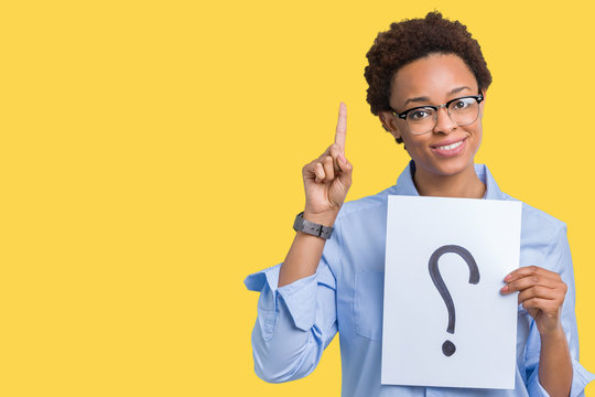 Young african american woman holding paper with question mark over isolated background surprised with an idea or question pointing finger with happy face, number one