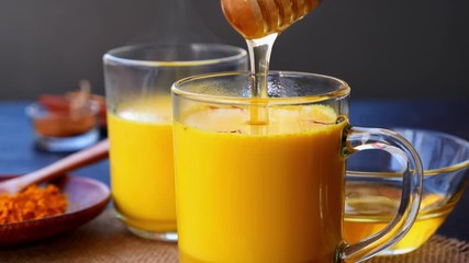 Sweetening saffron turmeric golden milk with honey. Honey is dripping from a wooden dipper in steaming  turmeric golden milk