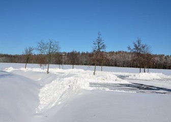 Parkplatz in verschneiter Winterlandschaft mit Schneewehen durch Winterdienst 