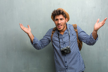 Young handsome traveler man wearing a straw hat, a backpack and a photo camera crazy and desperate,...