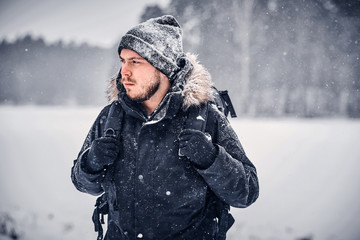 Portrait of a serious hiker guy with a backpack walking through a winter forest