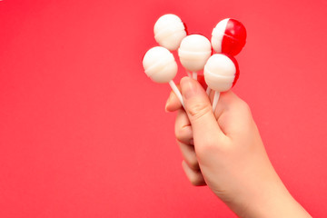 Lollipop in female hand on red background. Space for text or design.