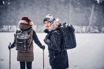Portrait of a young hiker guy with a backpack walking with his girlfriend through a winter woods