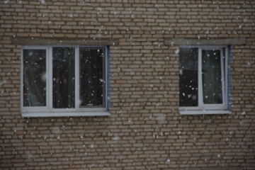 The wall of an old brick house on the background of snowfall - heating, preparation for winter, installation of plastic Windows