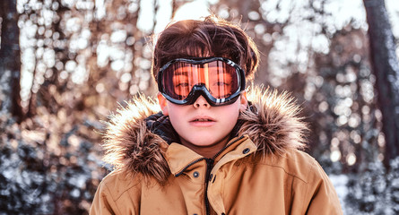 Portrait of a young snowboarder dressed in warm clothes and protective goggles standing in a snowy...