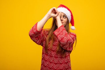 Young woman wearing santa hat making the gesture of a spyglass