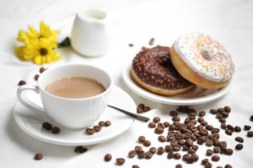 Obraz na płótnie Canvas cup of coffee and donuts on white table with yellow flowers