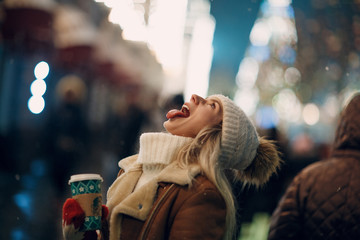 Young woman catches snowflakes by mouth