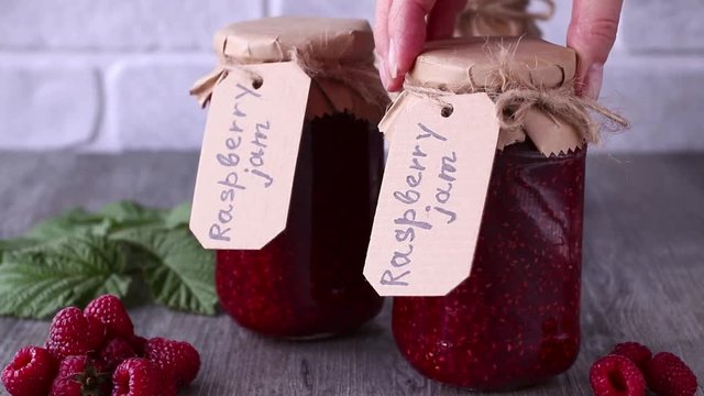 Raspberry jam in glass jars and fresh raspberries on a gray wooden table.