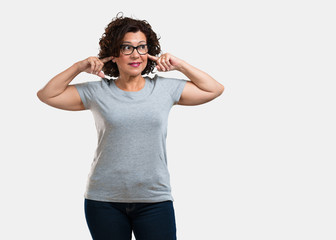 Middle aged woman covering ears with hands, angry and tired of hearing some sound