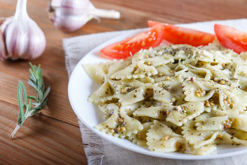 Farfalle pasta with pesto sauce, tomatoes and cheese on a linen tablecloth on a brown  wooden background.