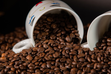 white cups with a pattern and grains of coffee on a black background