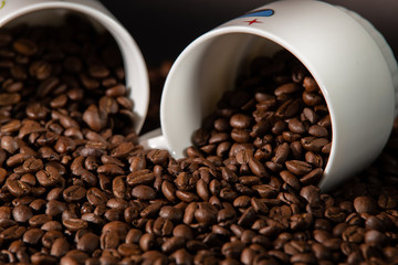 white cups with a pattern and grains of coffee on a black background