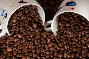 white cups with a pattern and grains of coffee on a black background