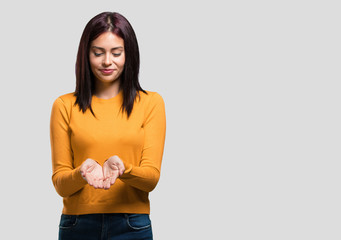 Young pretty woman holding something with hands, showing a product, smiling and cheerful, offering an imaginary object