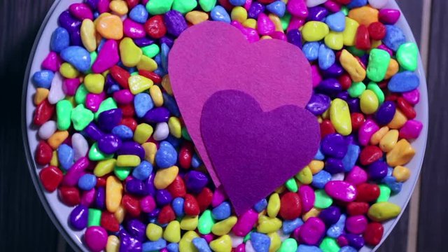 Two multicolored decorative hearts on a background of bright multi-colored pebbles. The concept of Valentine's Day and love.