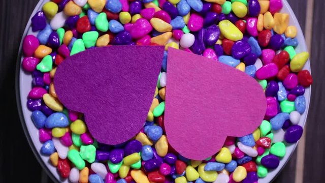 Two multicolored decorative hearts on a background of bright multi-colored pebbles. The concept of Valentine's Day and love.