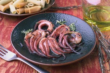 fried octopus tentacles in dish on veined wood in red
