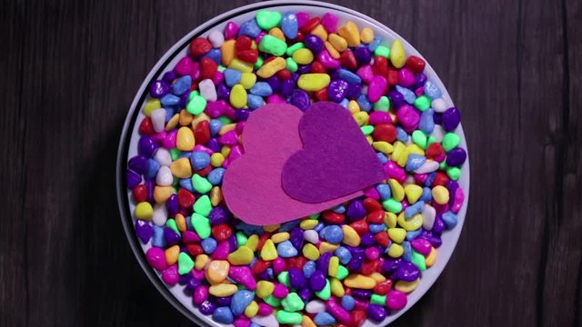 Two multicolored decorative hearts on a background of bright multi-colored pebbles. The concept of Valentine's Day and love.