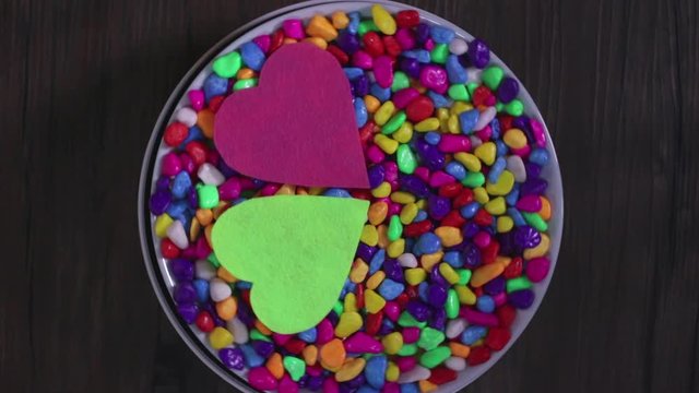 Two multicolored decorative hearts on a background of bright multi-colored pebbles. The concept of Valentine's Day and love.