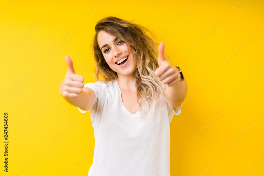 Wall mural young beautiful blonde woman over yellow background approving doing positive gesture with hand, thum