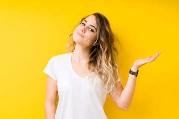 Young beautiful blonde woman over yellow background smiling cheerful presenting and pointing with palm of hand looking at the camera.