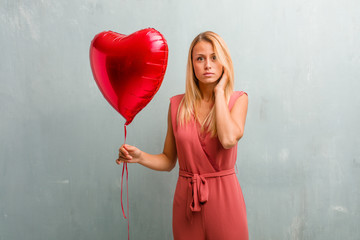 Portrait of young elegant blonde woman covering ears with hands, angry and tired of hearing some sound. Holding a red heart balloon.