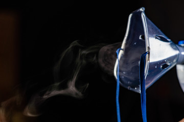 mask nebulizer produces a pair of drugs on a dark background. close-up of face mask