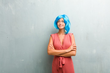 Portrait of young elegant blonde woman looking up, thinking of something fun and having an idea, concept of imagination, happy and excited. She is wearing a blue wig.