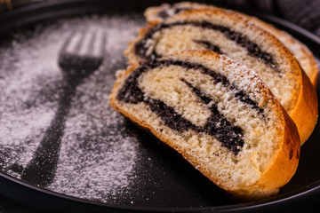 Poppy seed strudel on dark plate with silhouette of fork made by sugar