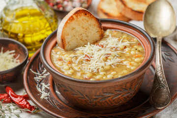 Thick soup with vegetables (carrots, onions, tomatoes), pasta, lentils, cheese and spices.  Minestrone. Olive oil and bread on the table. Italian cuisine. Selective focus