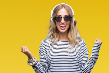 Fototapeta premium Beautiful young blonde woman wearing headphones and sunglasses over isolated background celebrating surprised and amazed for success with arms raised and open eyes. Winner concept.