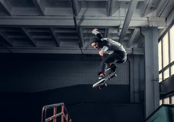 Afwasbaar fotobehang Skateboarder die hoog op minihelling springt bij skatepark binnen. © Fxquadro