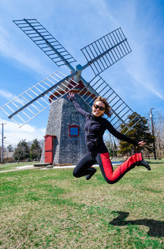Woman jumping in front of the Eastham Windmill. The historic old fashioned mill sits in a Cape Cod Park in Massachusetts. Fisheye lens view