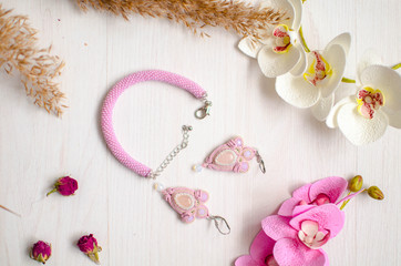 Beaded braselet and earrings set. Pink soutache jewelry with flowers on the white wooden background. Women accessories
