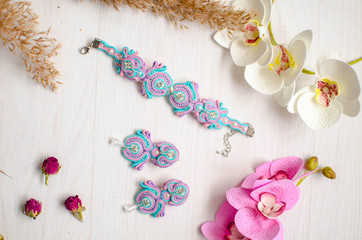 Beaded braselet and earrings set. Pink and blue soutache jewelry with flowers on the white wooden background. Women accessories