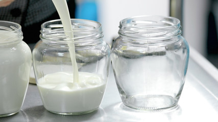 Close up glass jars filling with fresh milk. Milk pouring into glass container. Preparation of healthy yoghurt at home.