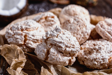 Delicious homemade coconut meringue type biscuits next to chopped coconut and coconut chips on a wooden table