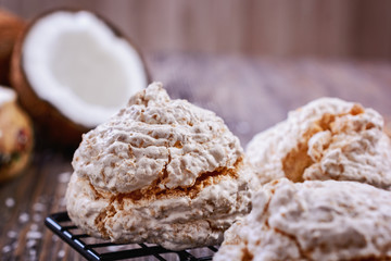 Delicious homemade coconut meringue type biscuits next to chopped coconut and coconut chips on a wooden table
