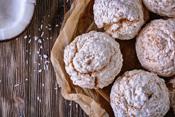 Delicious homemade coconut meringue type biscuits next to chopped coconut and coconut chips on a wooden table