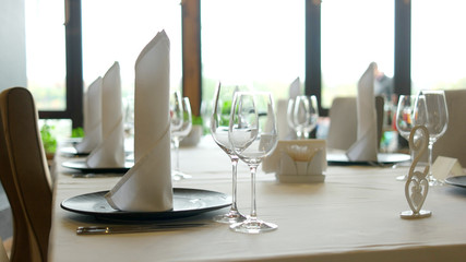 Table set in restaurant. Close up empty wine glasses, plates with napkins and cutlery on table in luxury restaurant. Table setting guide.