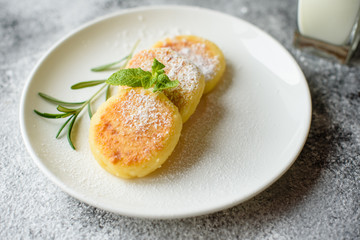 Tasty fresh cottage cheese pancakes on a white plate with a glass of milk on a concrete background. Healthy and diet breakfast