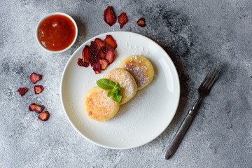 Tasty fresh cottage cheese pancakes on a white plate with a glass of milk on a concrete background. Healthy and diet breakfast