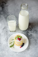 Tasty fresh cottage cheese pancakes on a white plate with a glass of milk on a concrete background. Healthy and diet breakfast