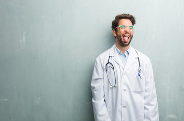 Young friendly doctor man against a grunge wall with a copy space expression of confidence and emotion, fun and friendly, showing tongue as a sign of play or fun