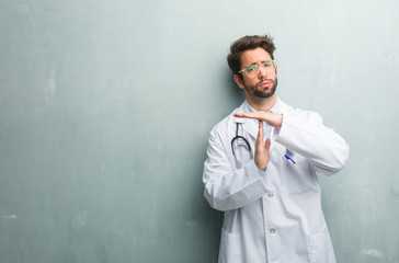 Young friendly doctor man against a grunge wall with a copy space tired and bored, making a timeout...