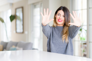 Young beautiful woman wearing winter sweater at home showing and pointing up with fingers number ten while smiling confident and happy.